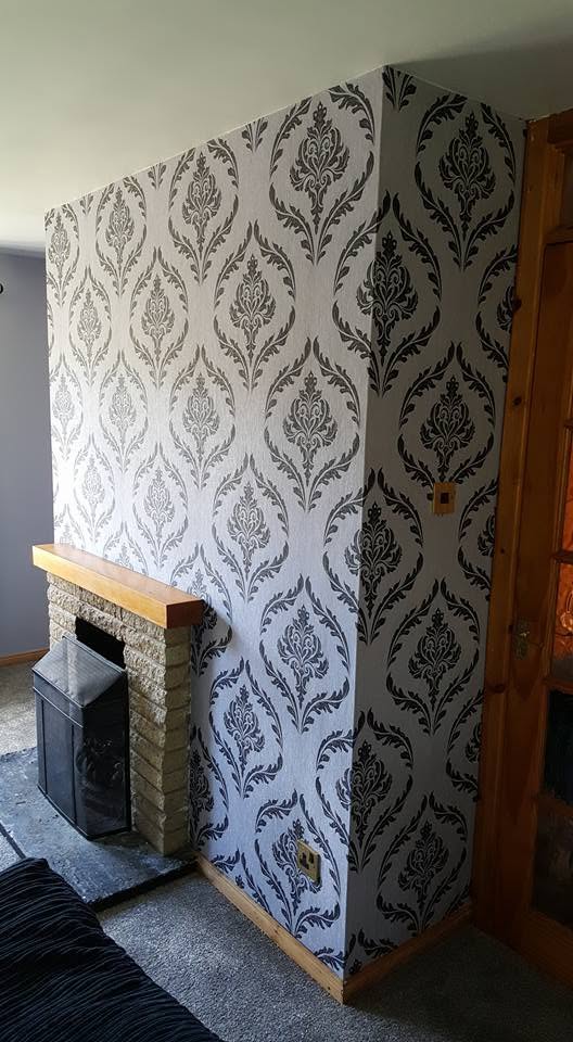 Large damask wallpaper matched around a fireplace and its outer corner